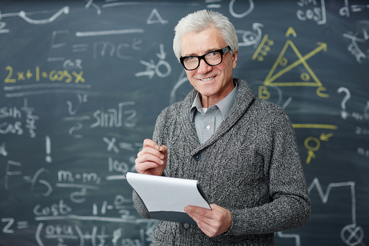 An older man smiling in front of a chalkboard covered in mathematical equations